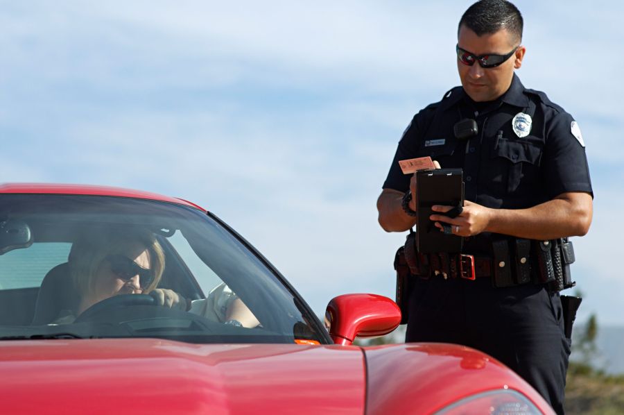 A police officer issuing a traffic ticket to a driver in a red sports car.