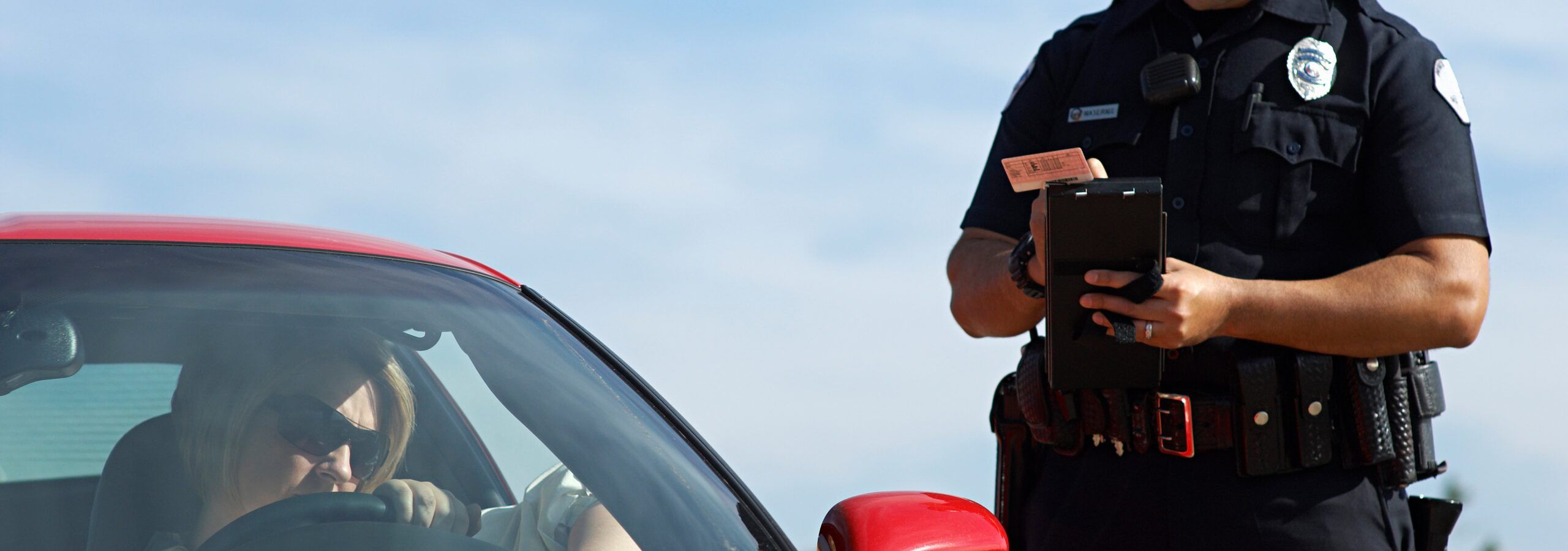A police officer issuing a traffic ticket to a driver in a red sports car.