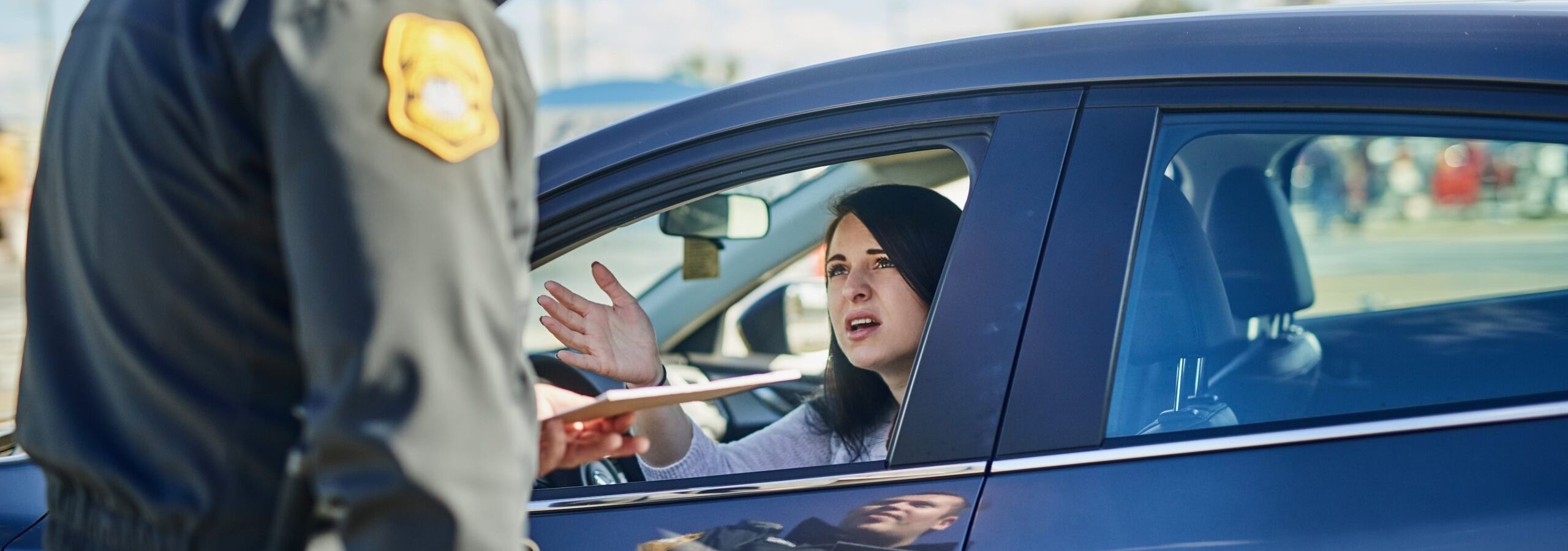 A police officer standing beside a car, speaking to a woman in the driver's seat who appears to be explaining something.