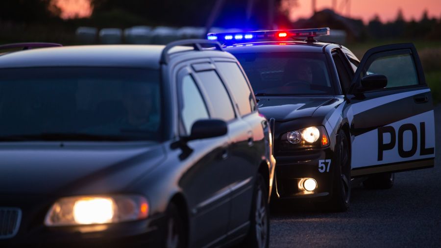 A police car with flashing lights pulls over a dark SUV on the road at sunset.